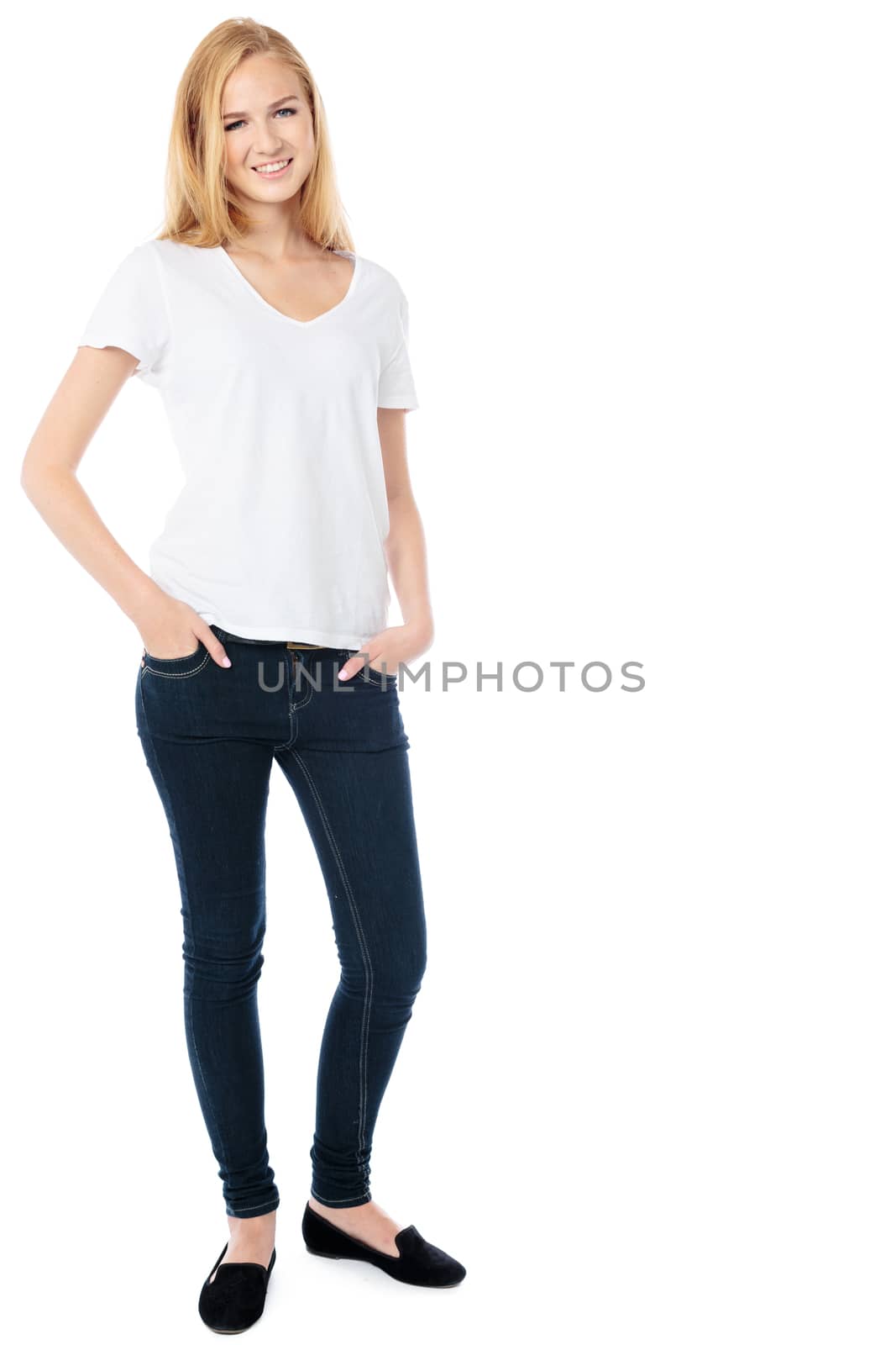 Slender friendly young woman in trendy jeans standing relaxing with her hands in her pockets smiling at the camera, isolated on white