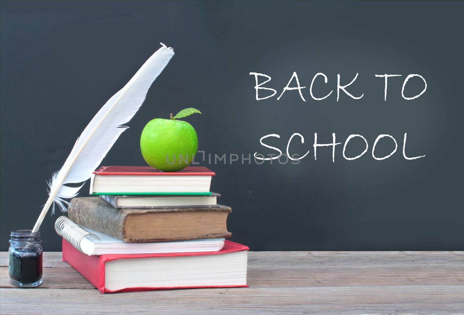 Back to school written on a blackboard with a stack of books, apple and quill pen