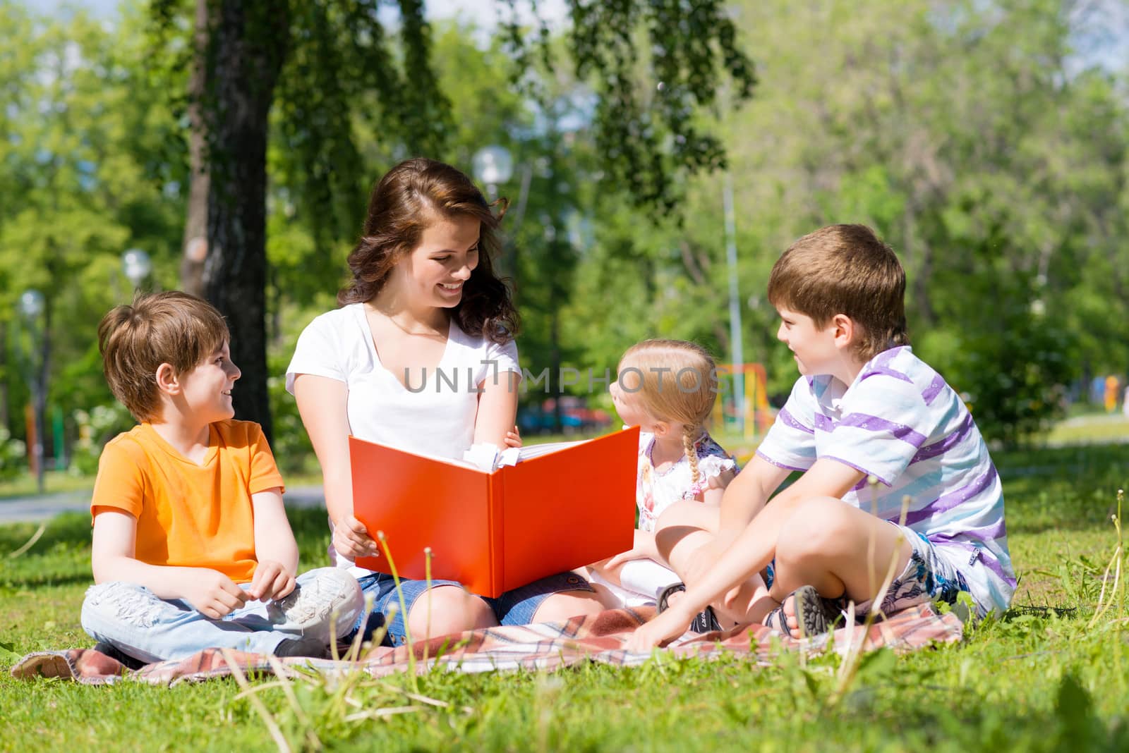 teacher reads a book to children in a summer park by adam121