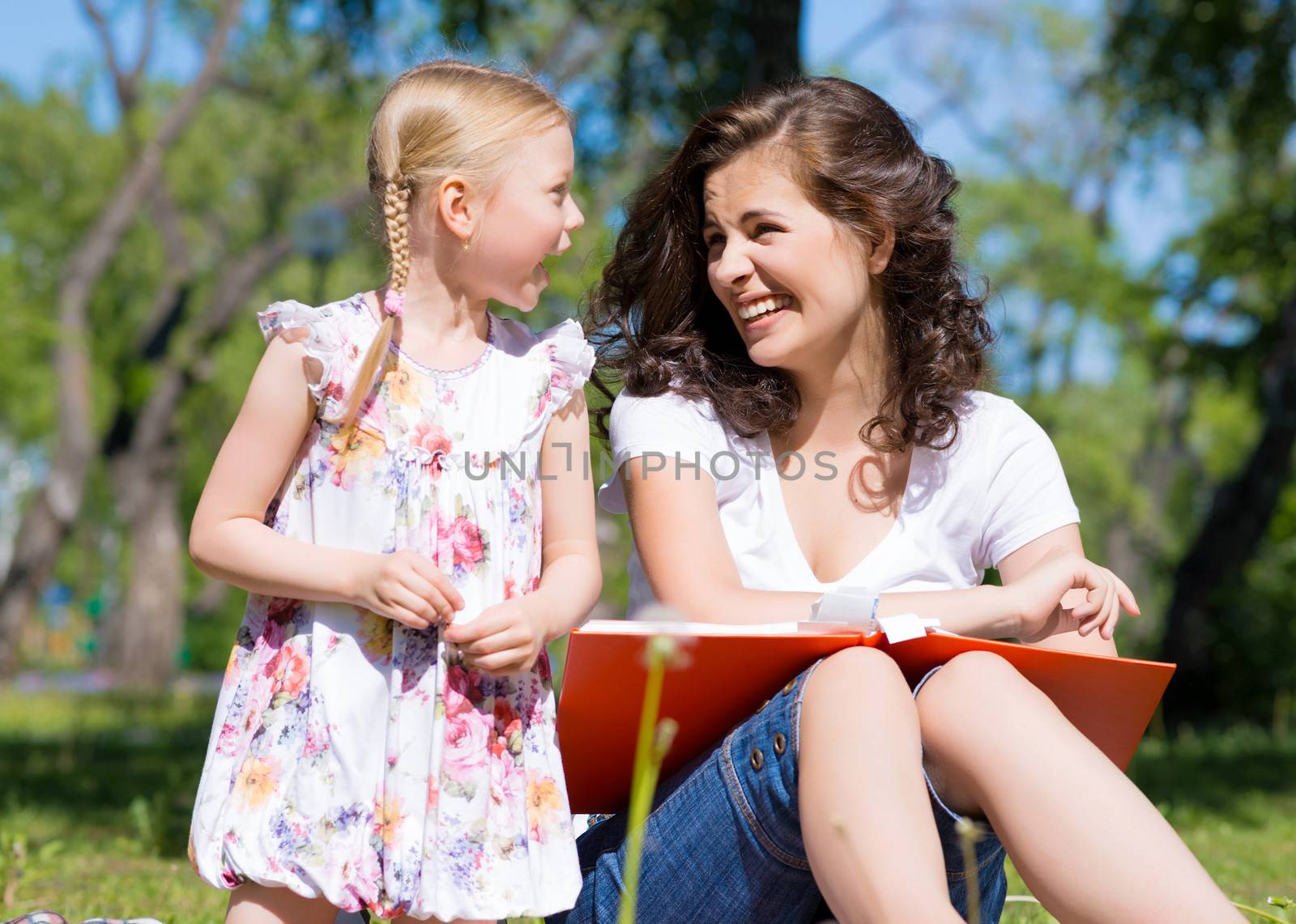 girl with the teacher reading a book together in the summer park