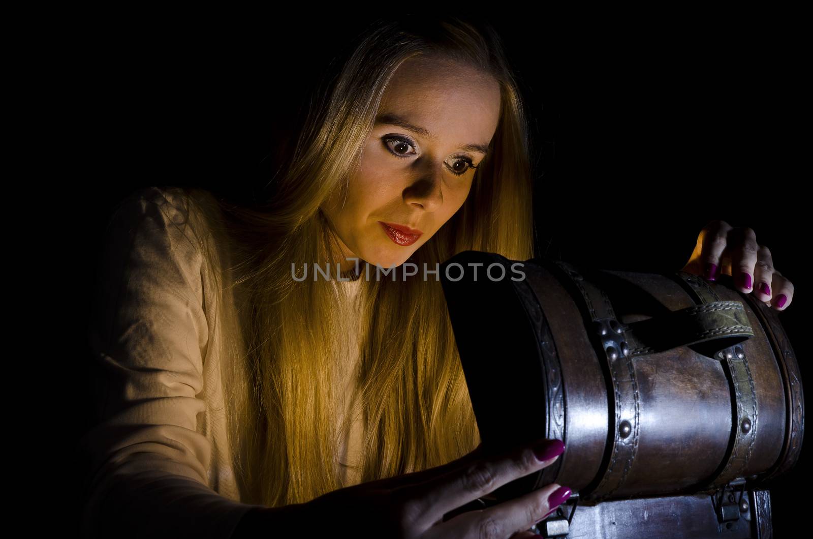 woman secretly opening a small chest in the dark with lights coming from it and falling on her face