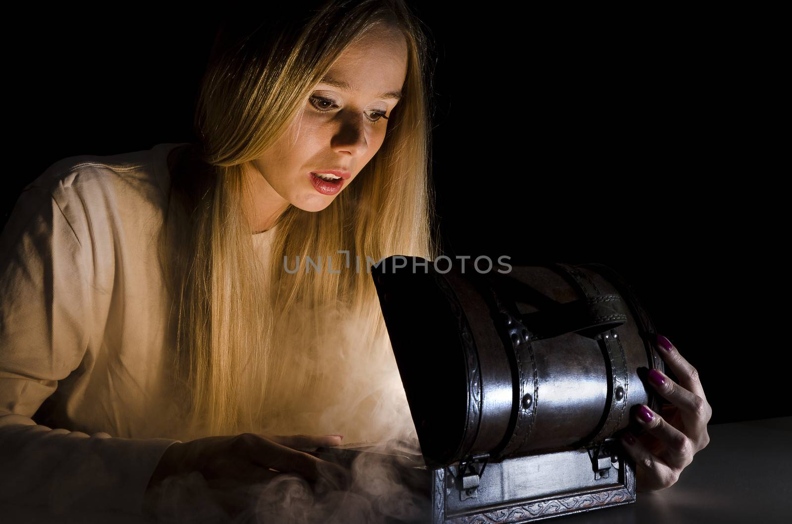 woman secretly opening a small chest in the dark with smoke and lights coming from it and falling on her face