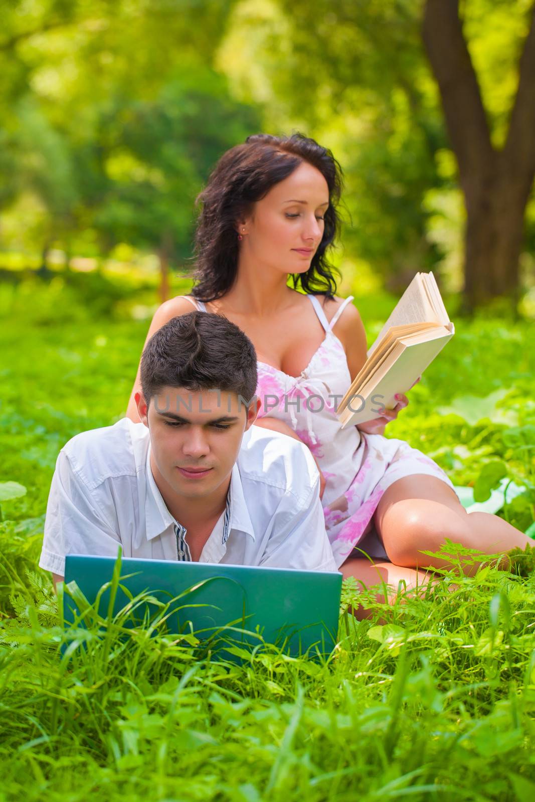 couple lying with laptop and book at park