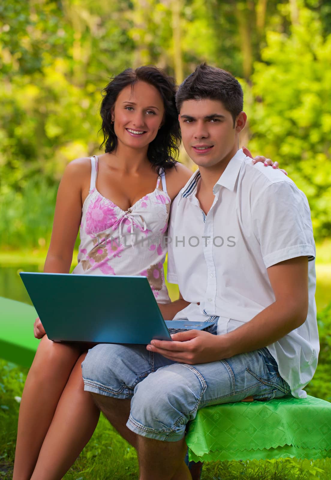 couple sitting with laptop in park by mihalec