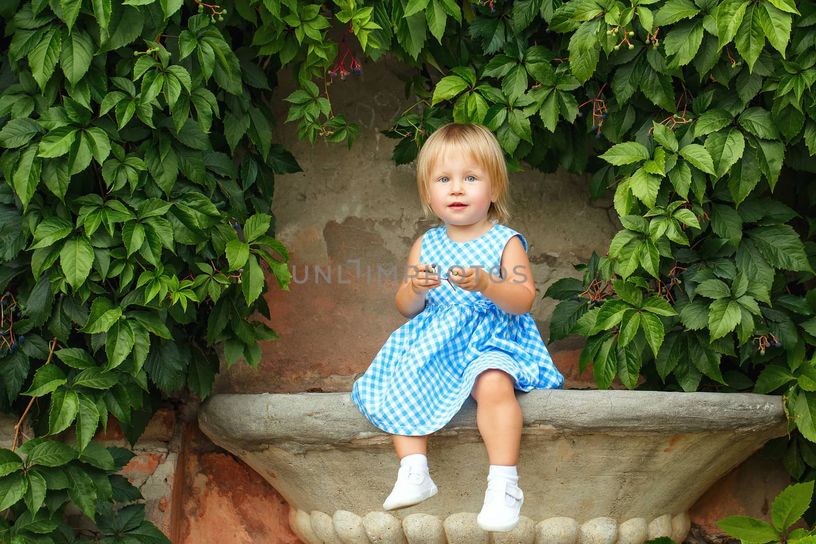 Little blonde girl on a background of green grape leaves
