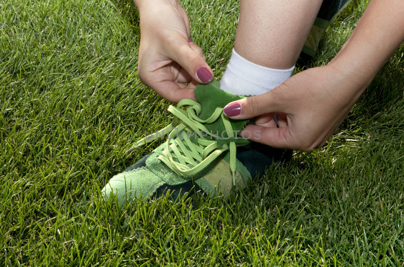 woman ties laces on green shoes by ssuaphoto