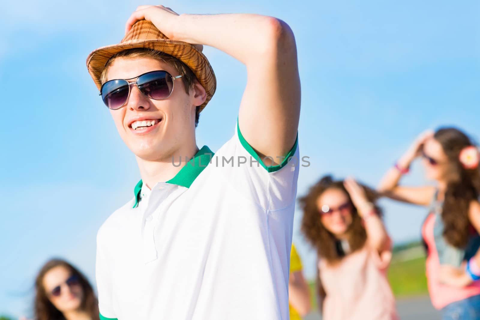 young man in sunglasses, a hat holds a hand on a background of blue sky and friends