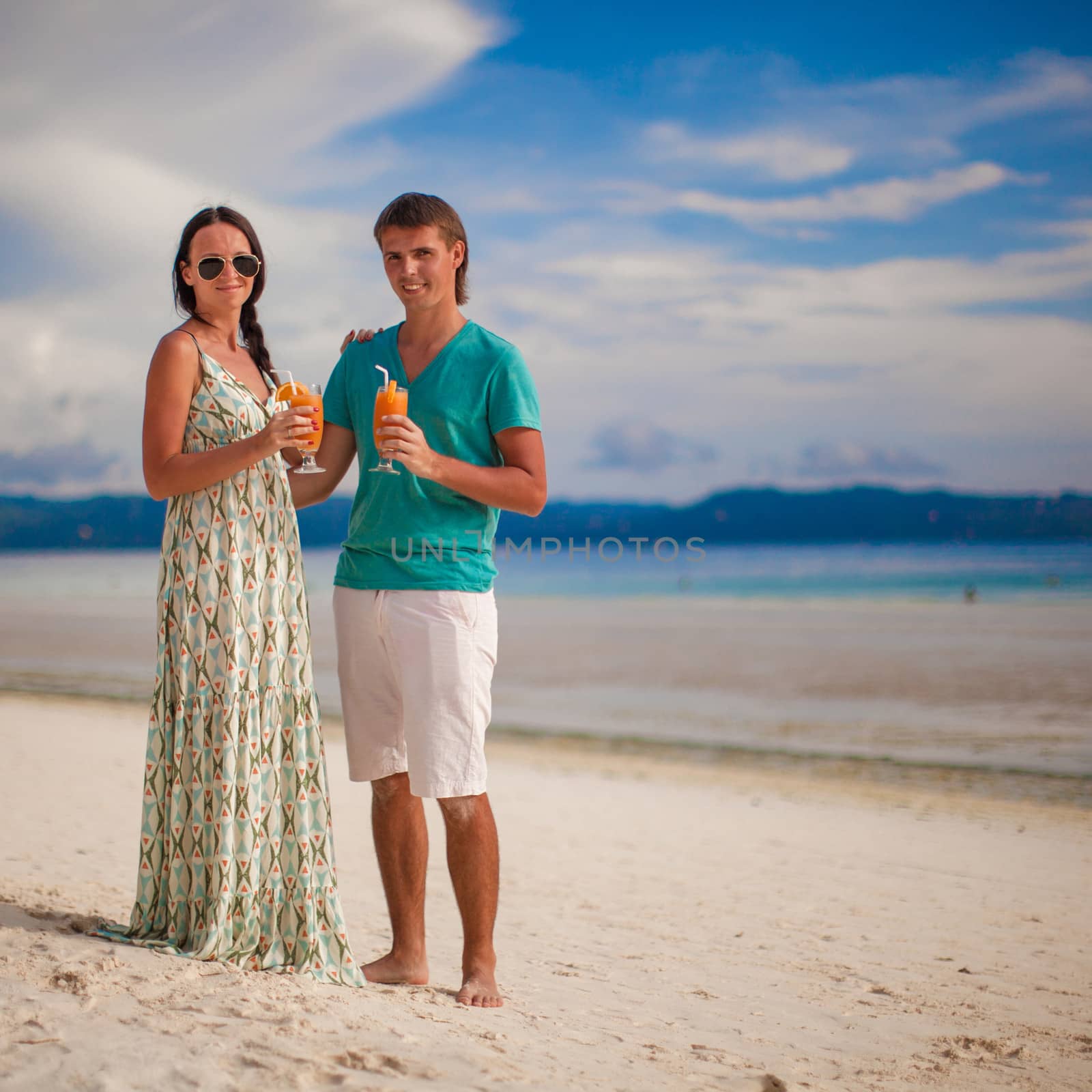 Young romantic couple relaxing with two cocktails on sandy beach by travnikovstudio