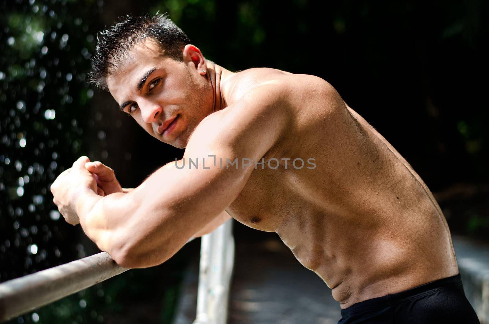 Attractive young muscleman outdoors, leaning on metal hand railing