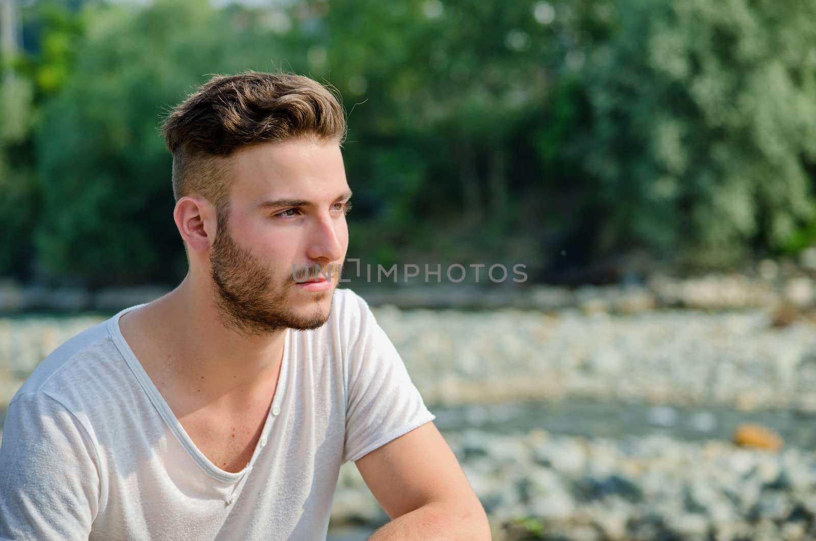 Portrait of handsome young man outdoors in nature, looking to a side