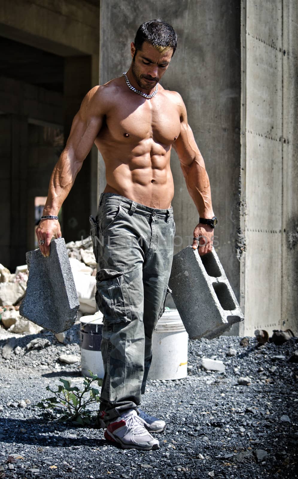 Sexy construction worker shirtless showing muscular body, holding big bricks