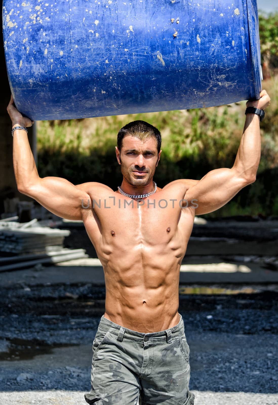 Hot, shirtless, muscular construction worker carrying big barrel over his head