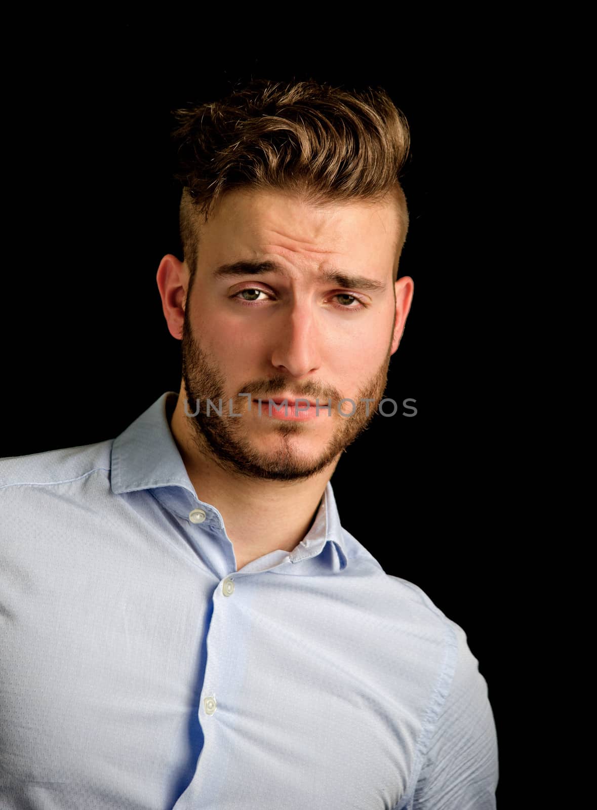Handsome young man portrait with doubtful, unsure expression, isolated on black background