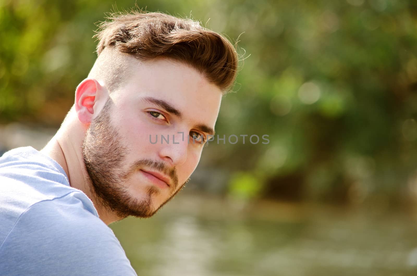 Portrait of handsome young man outdoors in nature, looking in camera