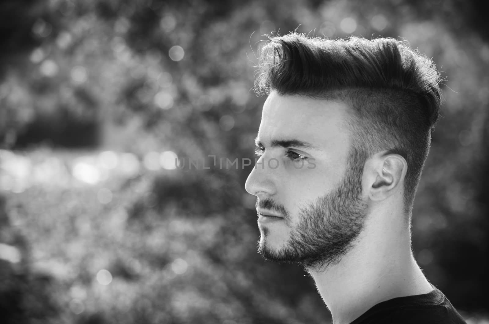 Profile portrait of handsome young man outdoors in nature, looking to a side, black and white shot