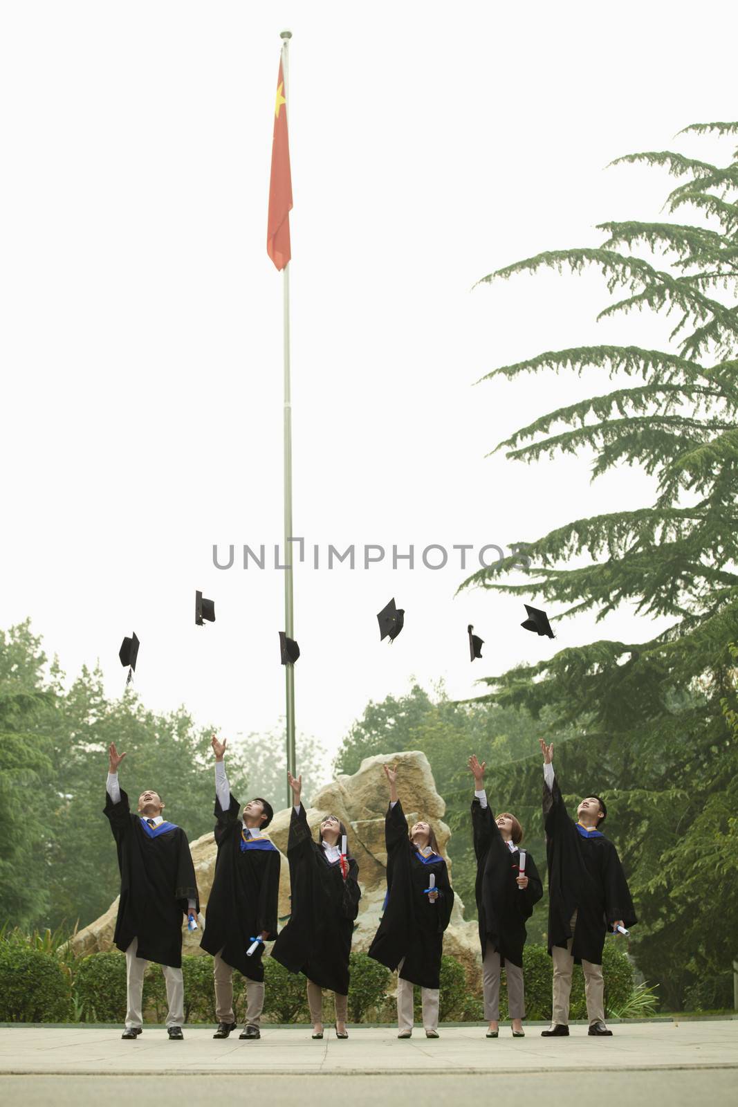 Young Group of University Graduates Throwing Mortarboards in the Air, Vertical