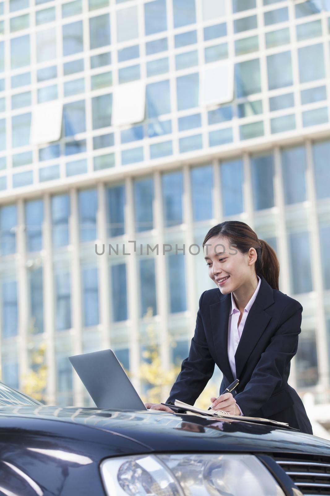 Businesswoman Standing by Car Using Laptop and Writing by XiXinXing