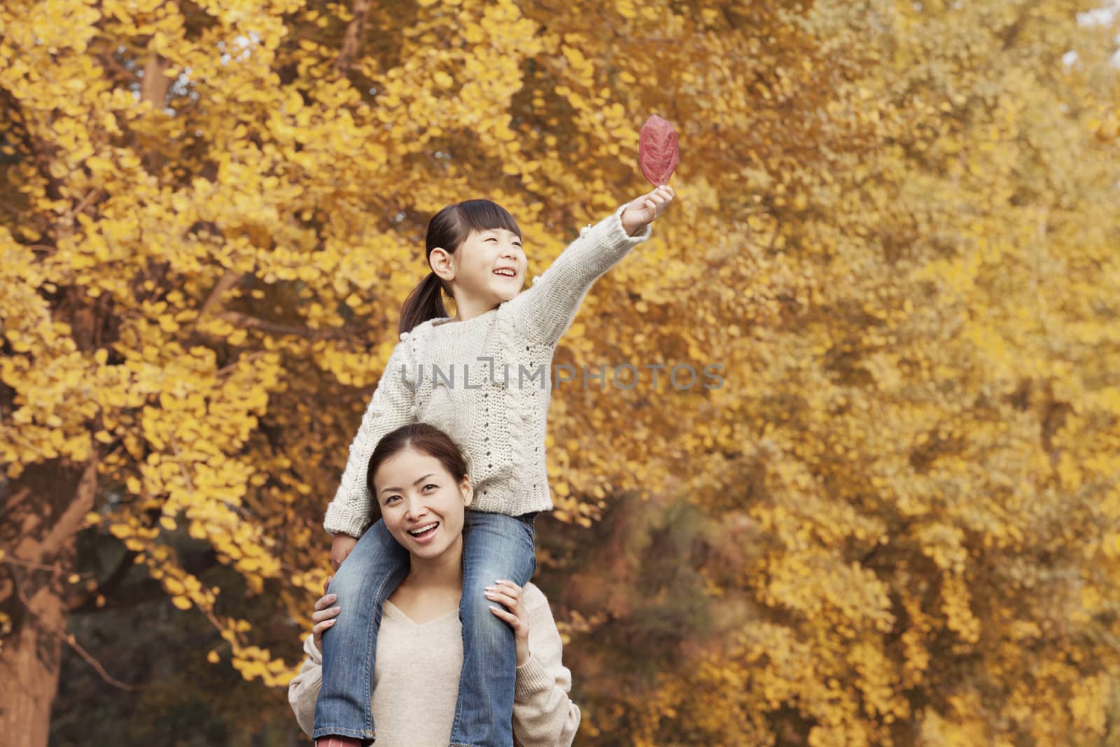 Daughter Riding Piggy-Back on Mother's Shoulders Enjoying Autumn Leaves by XiXinXing