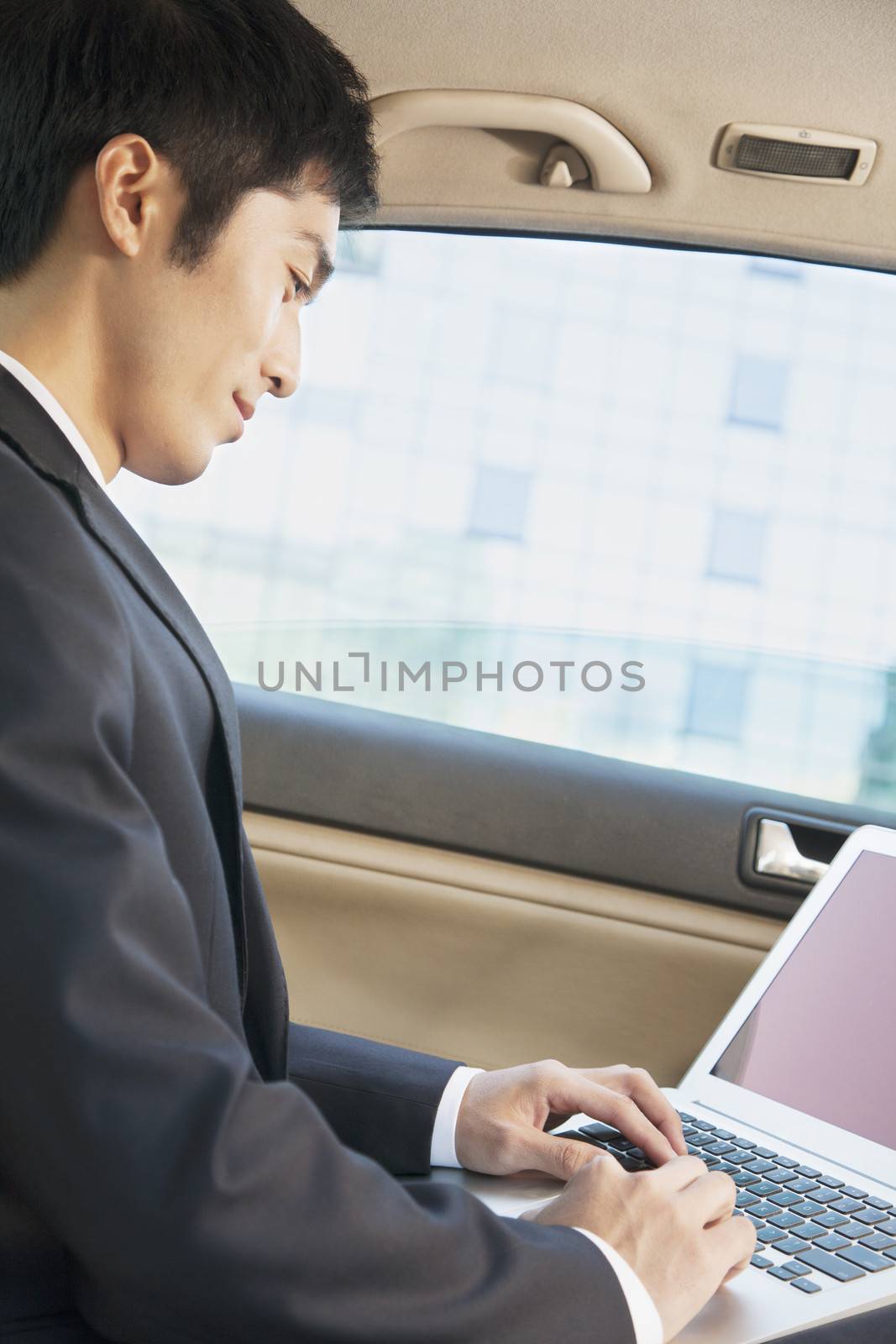  Businessman in Back Seat of Car Typing on Laptop