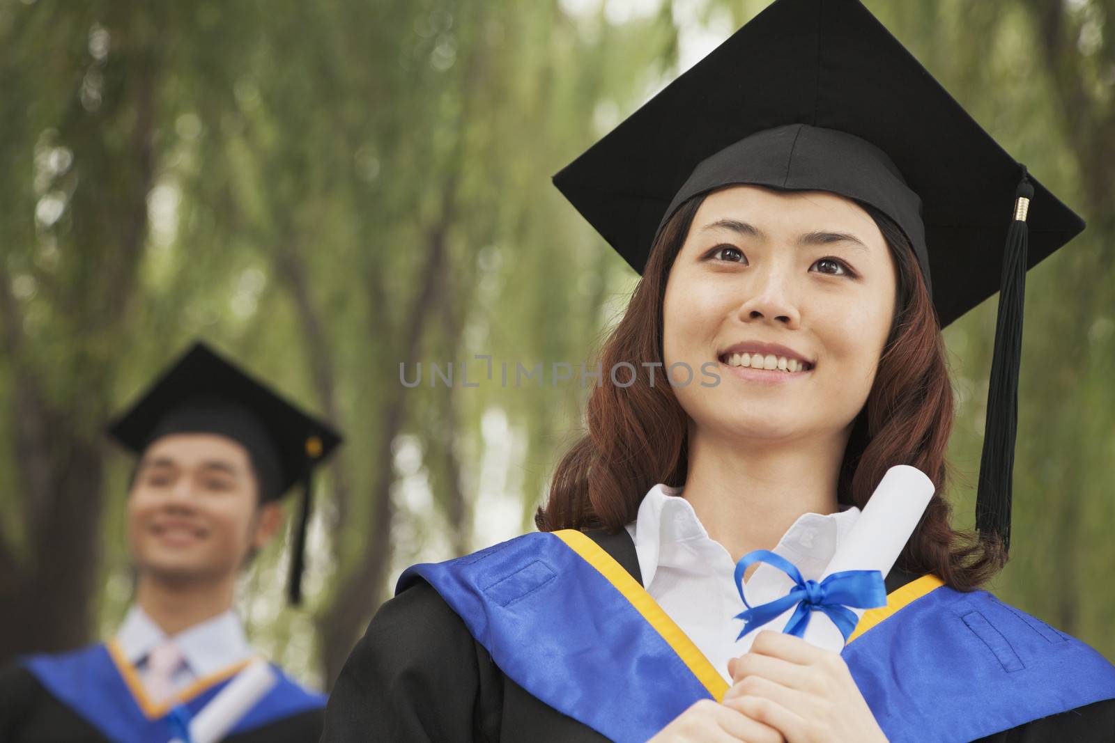 Two Young University Graduates Holding Diplomas, Woman in Front by XiXinXing