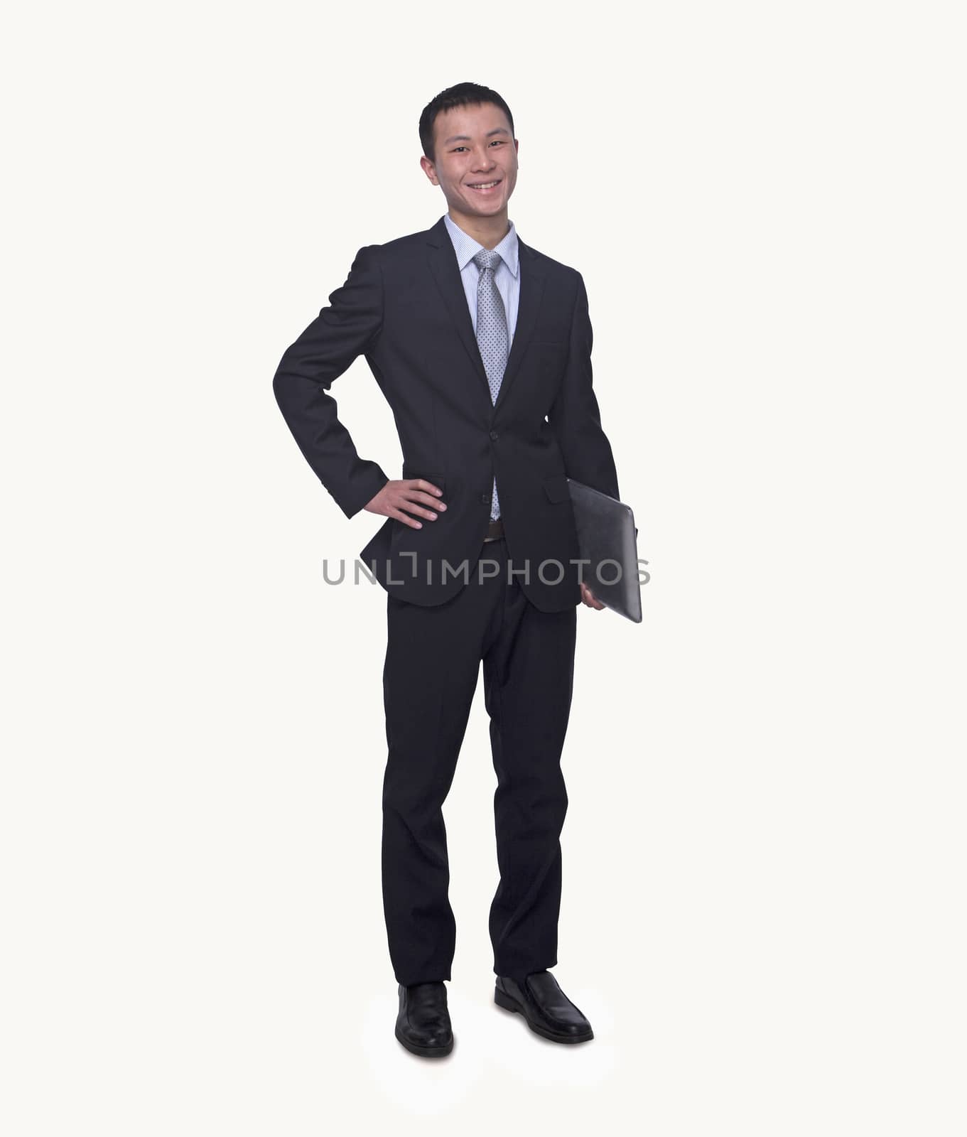 Portrait of smiling young businessman holding a laptop, hand on hip, studio shot