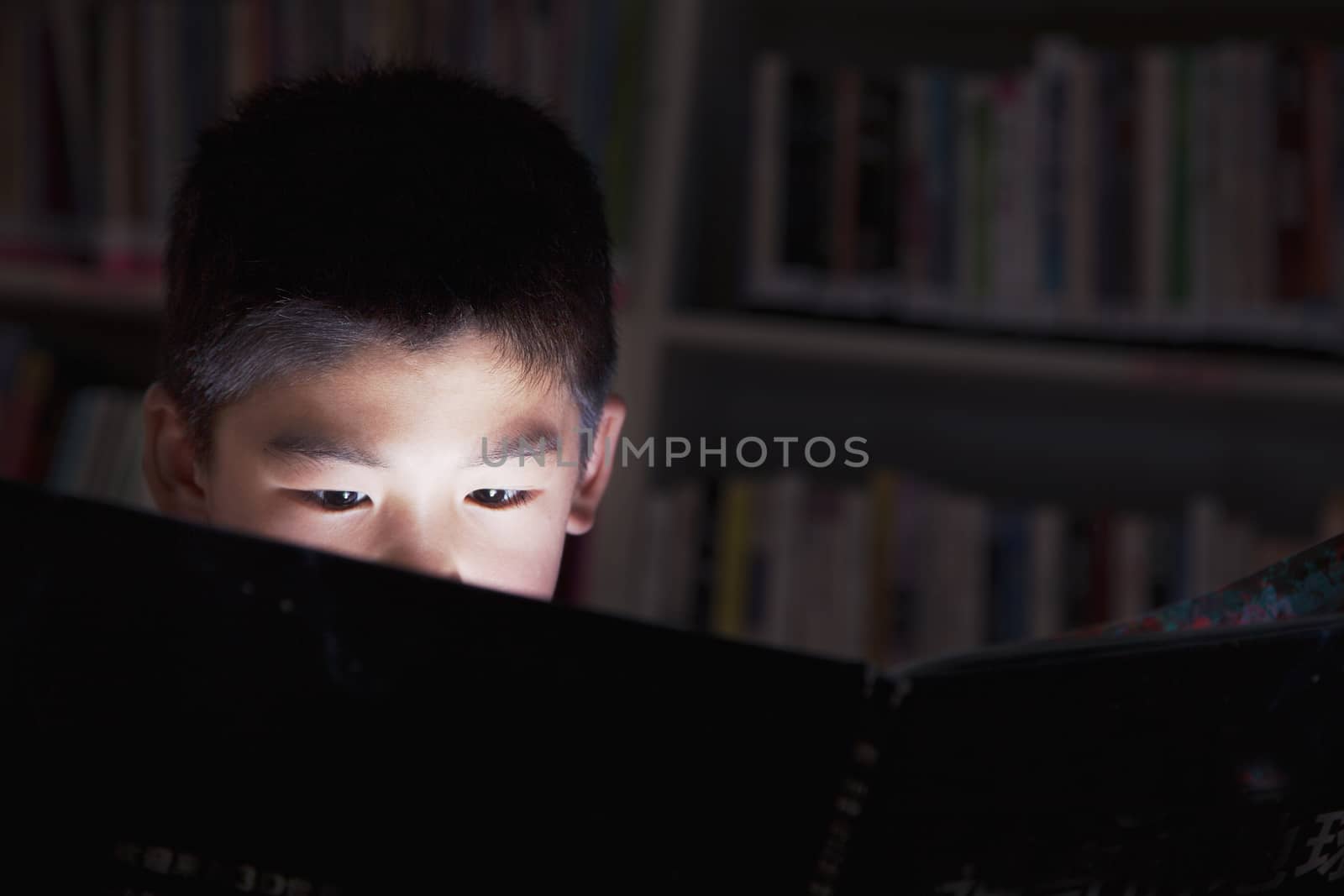Close up of a schoolboy reading a book with his face lit up