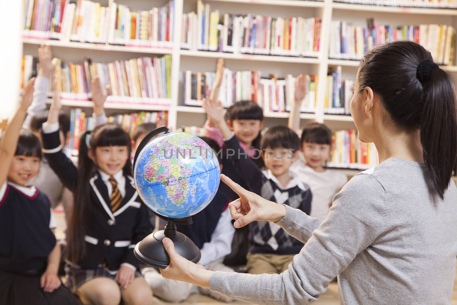 Teacher teaching geography to schoolchildren with a globe by XiXinXing