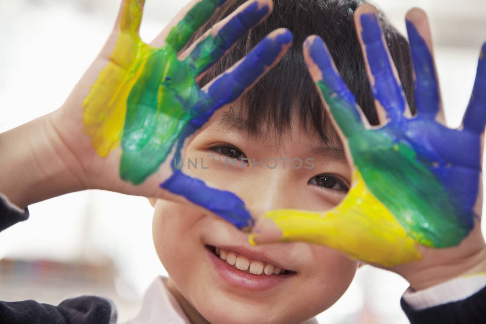 Portrait of smiling schoolboy finger painting, close up on hands by XiXinXing