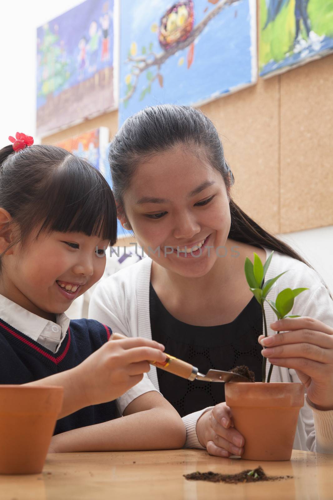 Teacher and schoolgirl planting plants into flowerpots