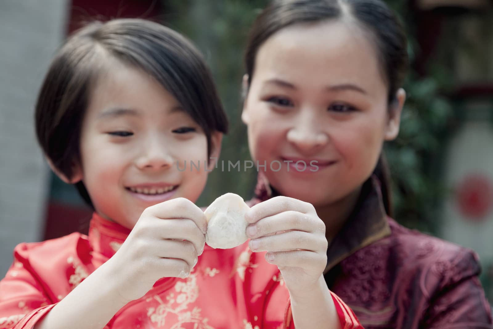 Mother and daughter making dumplings in traditional clothing, close up