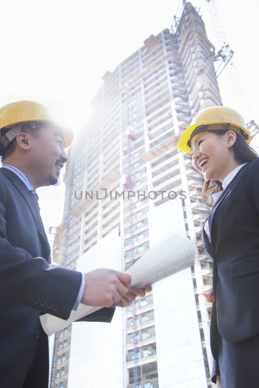 Two architects smiling at a construction site holding blueprint by XiXinXing