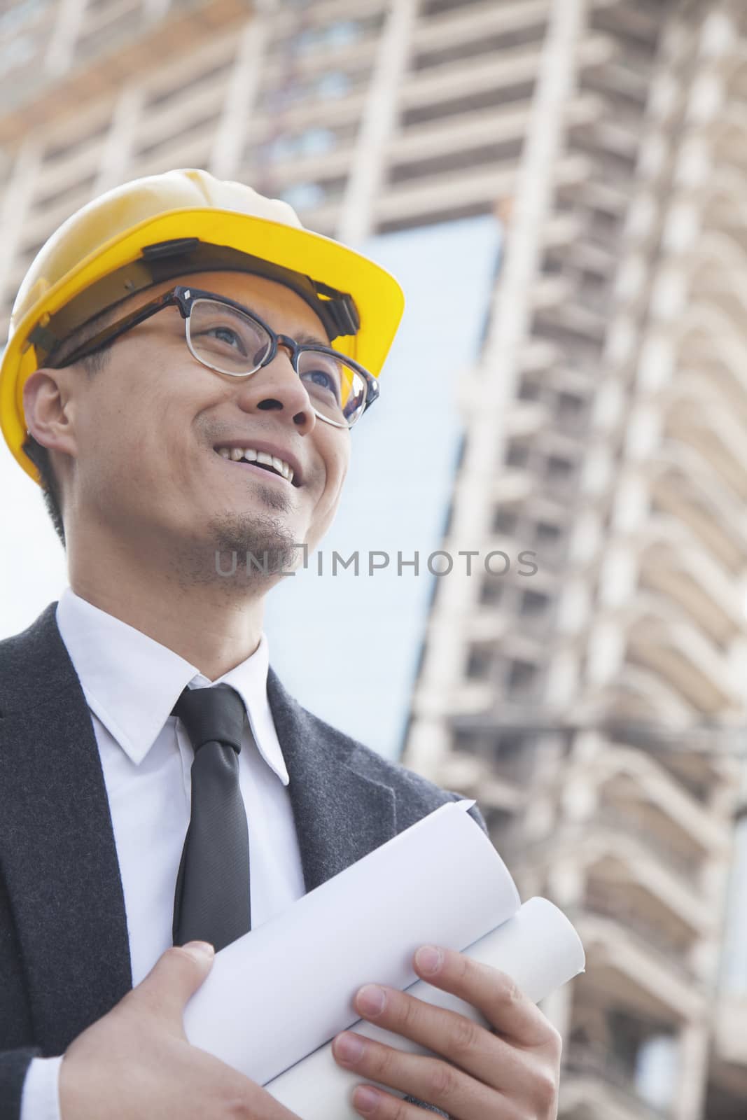Portrait of male architect on site carrying blueprints