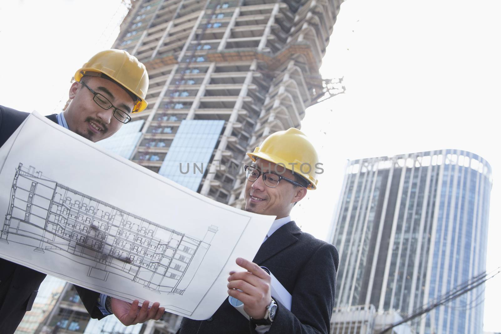 Architects looking at blueprint on construction site, Beijing by XiXinXing