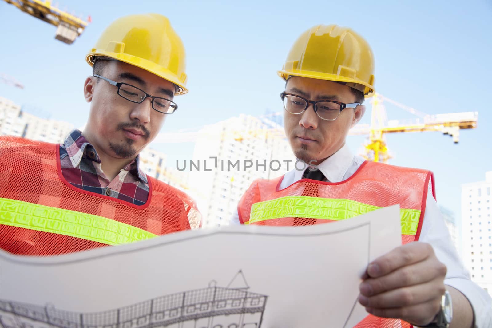 Two architects looking at a blueprint outdoors at a construction site