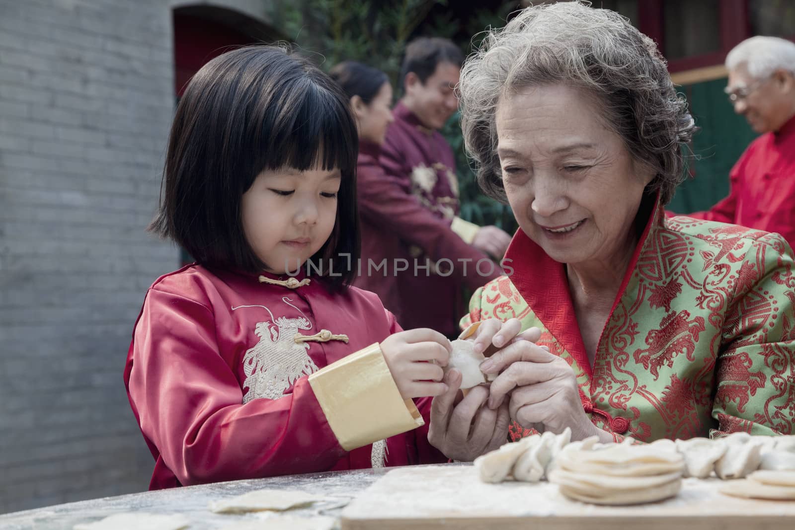 Grandmother and granddaughter making dumplings in traditional clothing