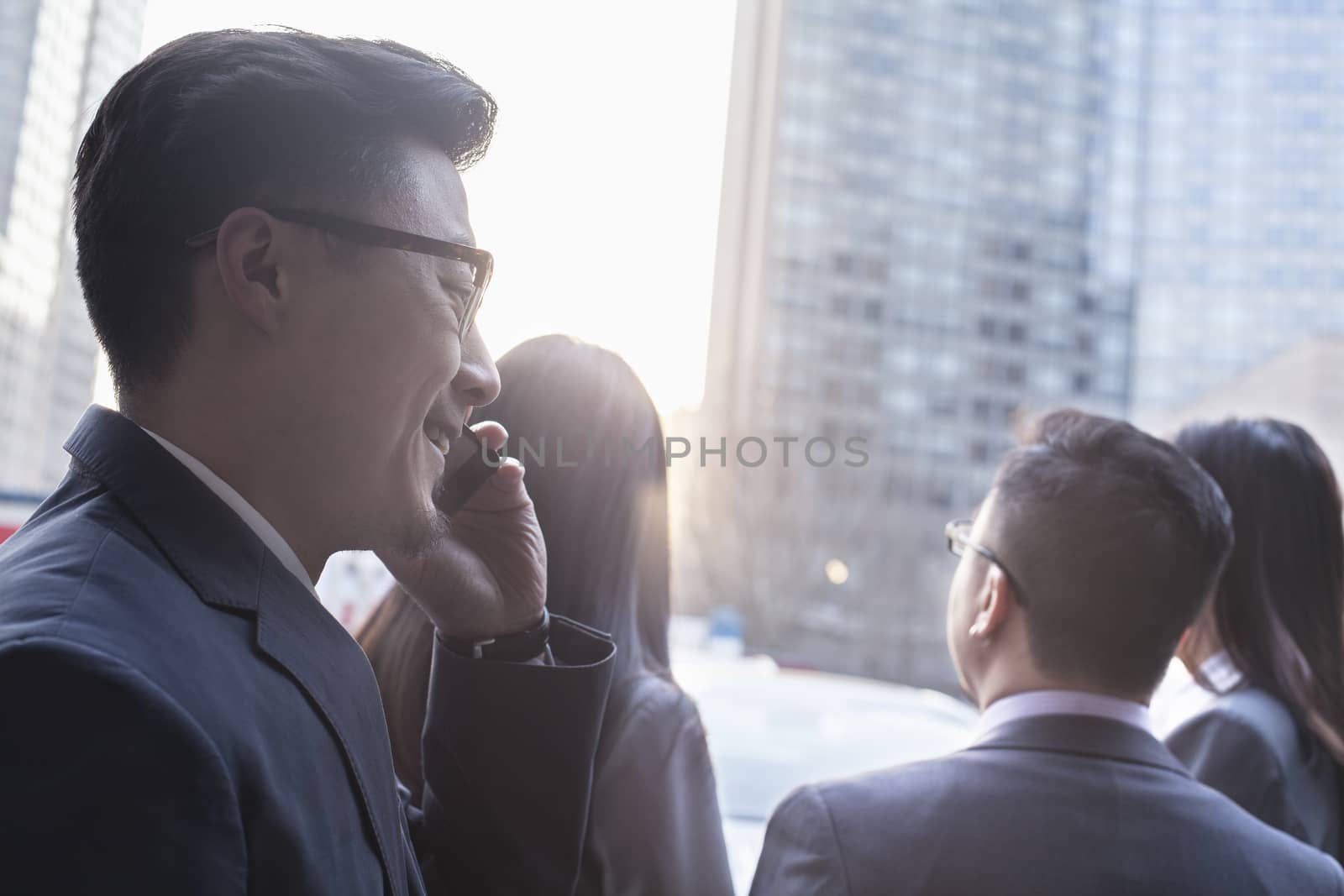 Businessman on the phone with colleagues in the background by XiXinXing