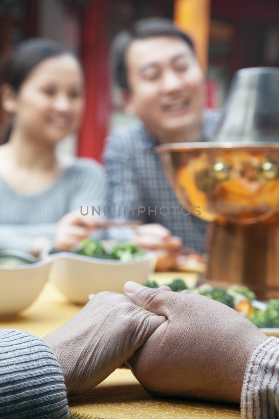 Senior couple holding hands at a family meal by XiXinXing