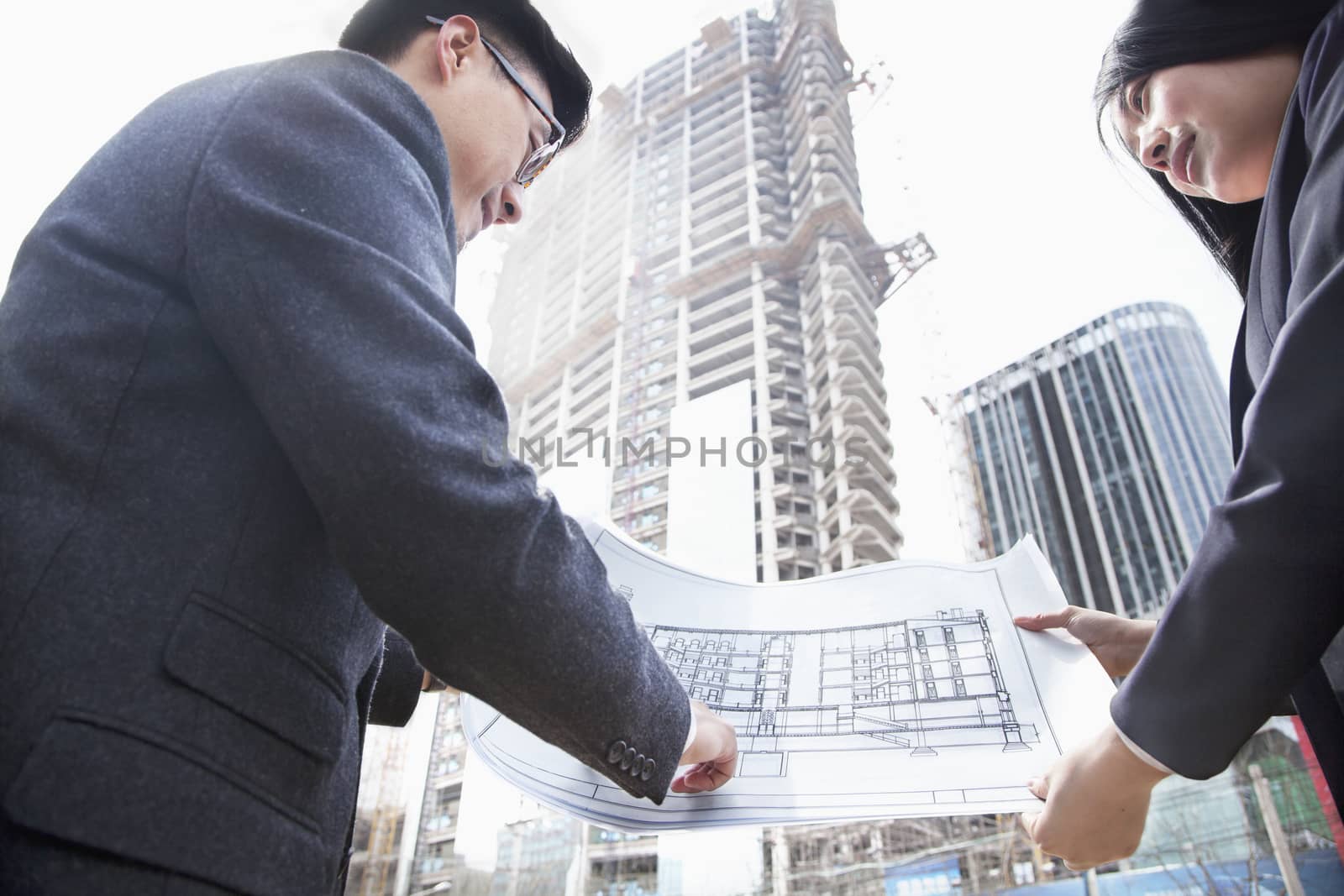Two architects looking at blueprint at a construction site