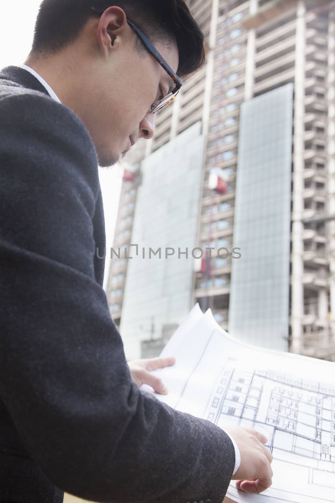 Architect looking at blueprint at a construction site by XiXinXing