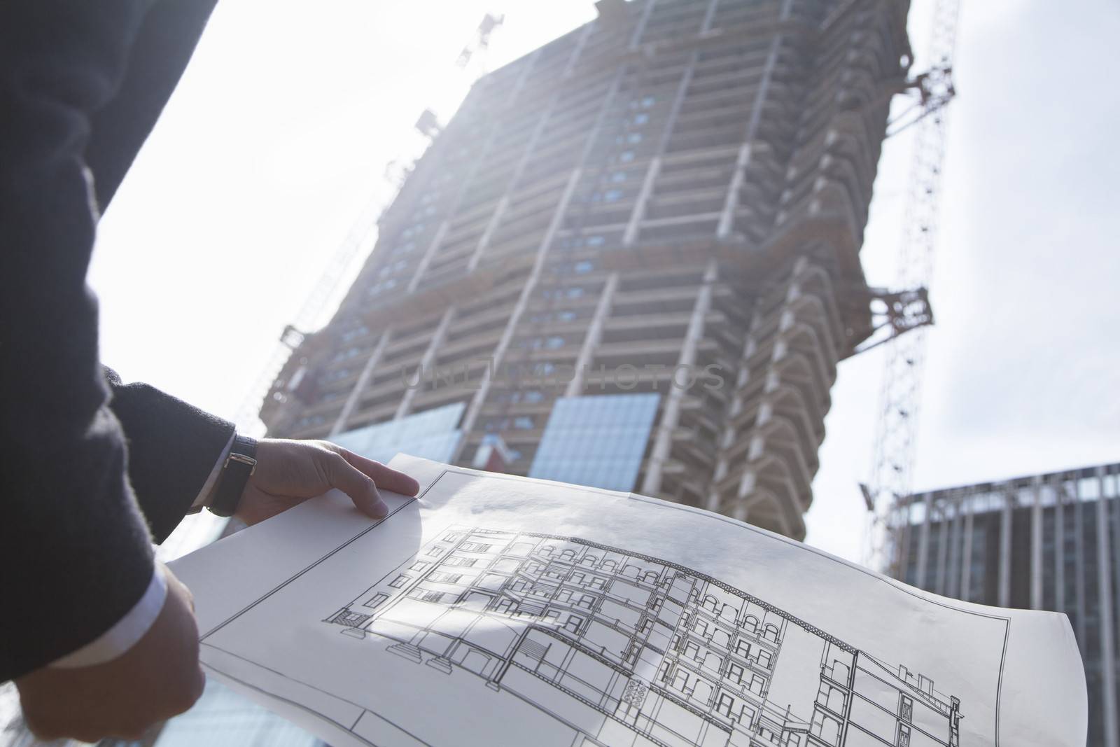 Architect holding blueprint of building at a construction site, midsection