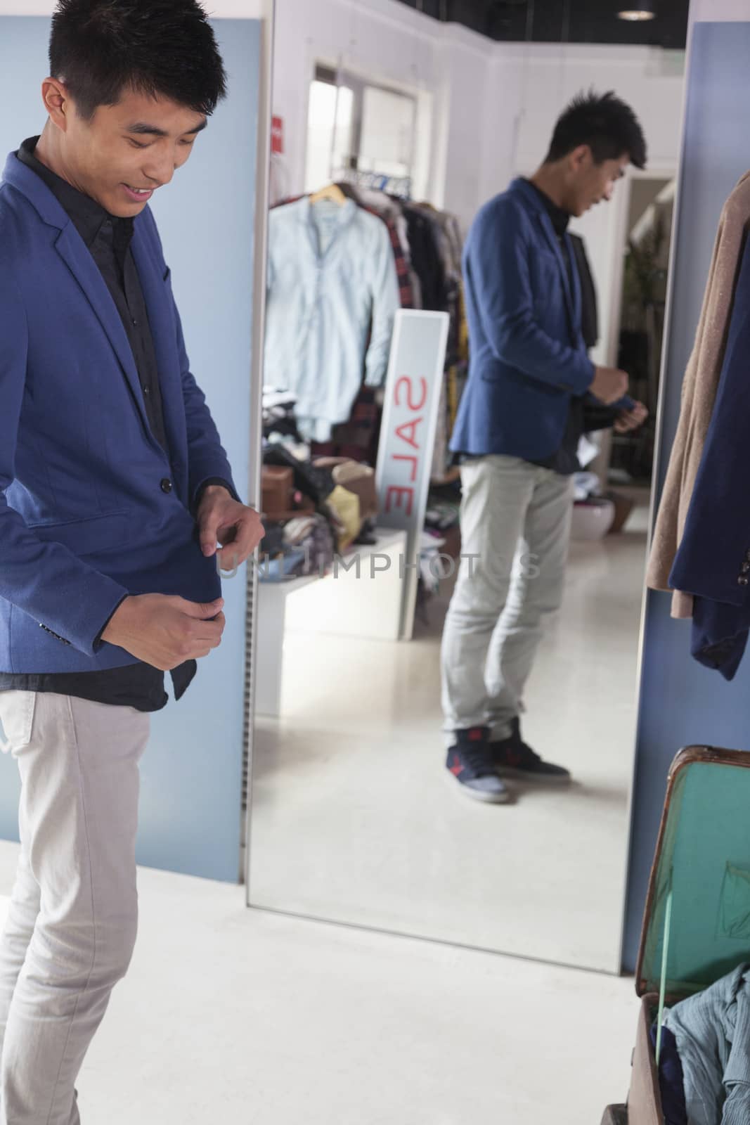 Young man trying on jacket at fashion store by XiXinXing