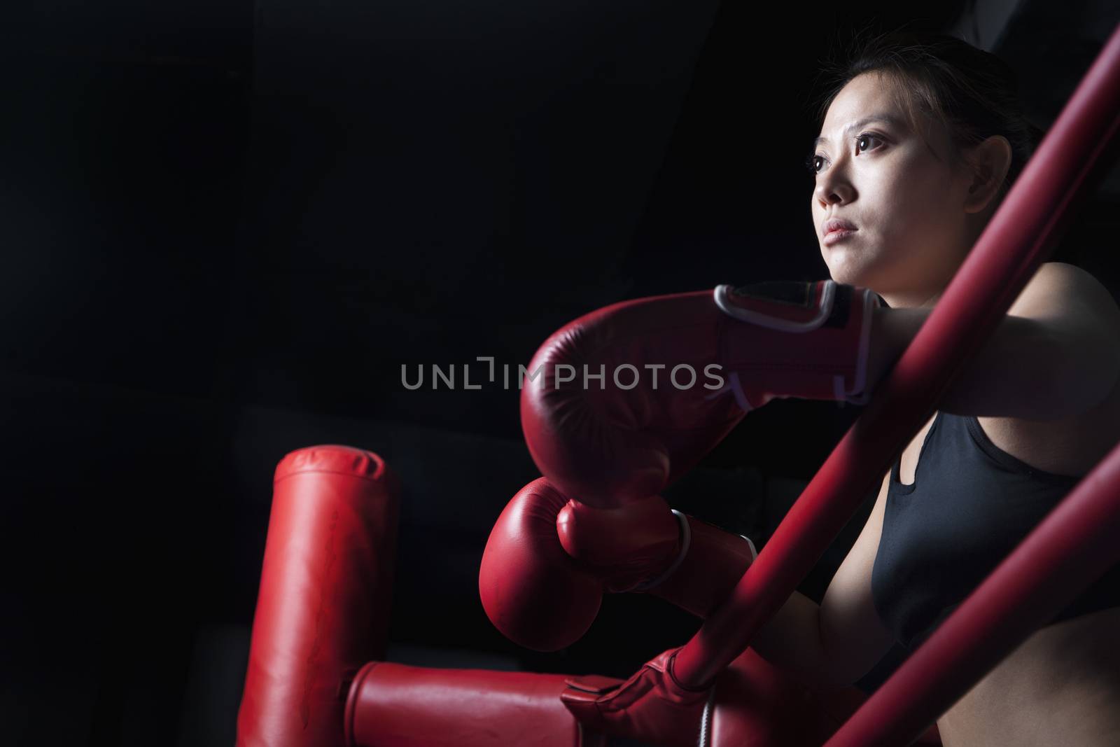 Serious female boxer resting her elbows on the ring side, looking away, low angle view