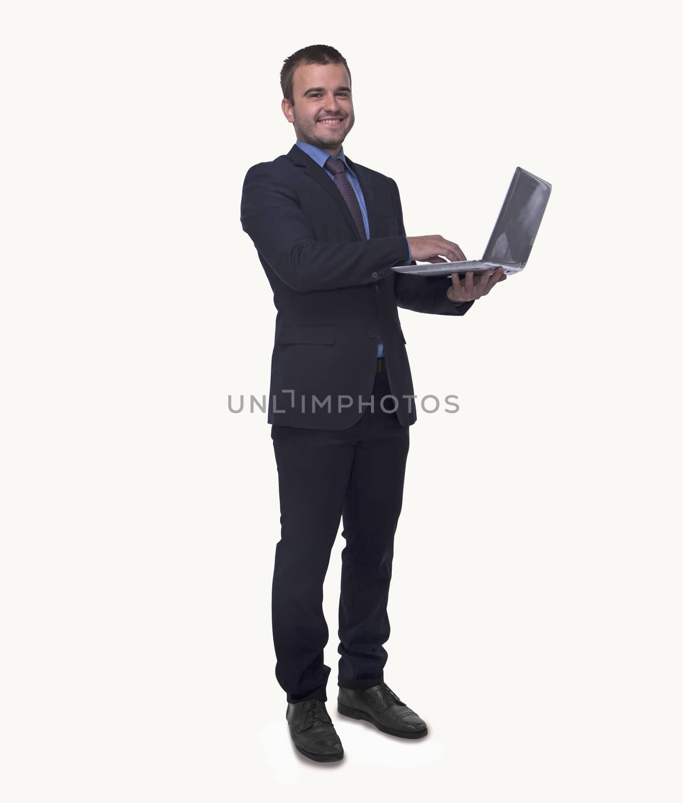 Portrait of smiling young businessman holding an open laptop, full length, studio shot by XiXinXing