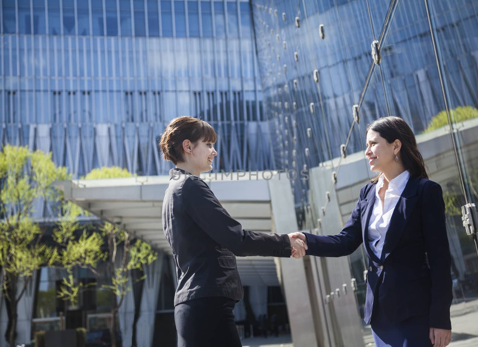 Two smiling young businesswomen shaking hands outdoors in Beijing, China by XiXinXing