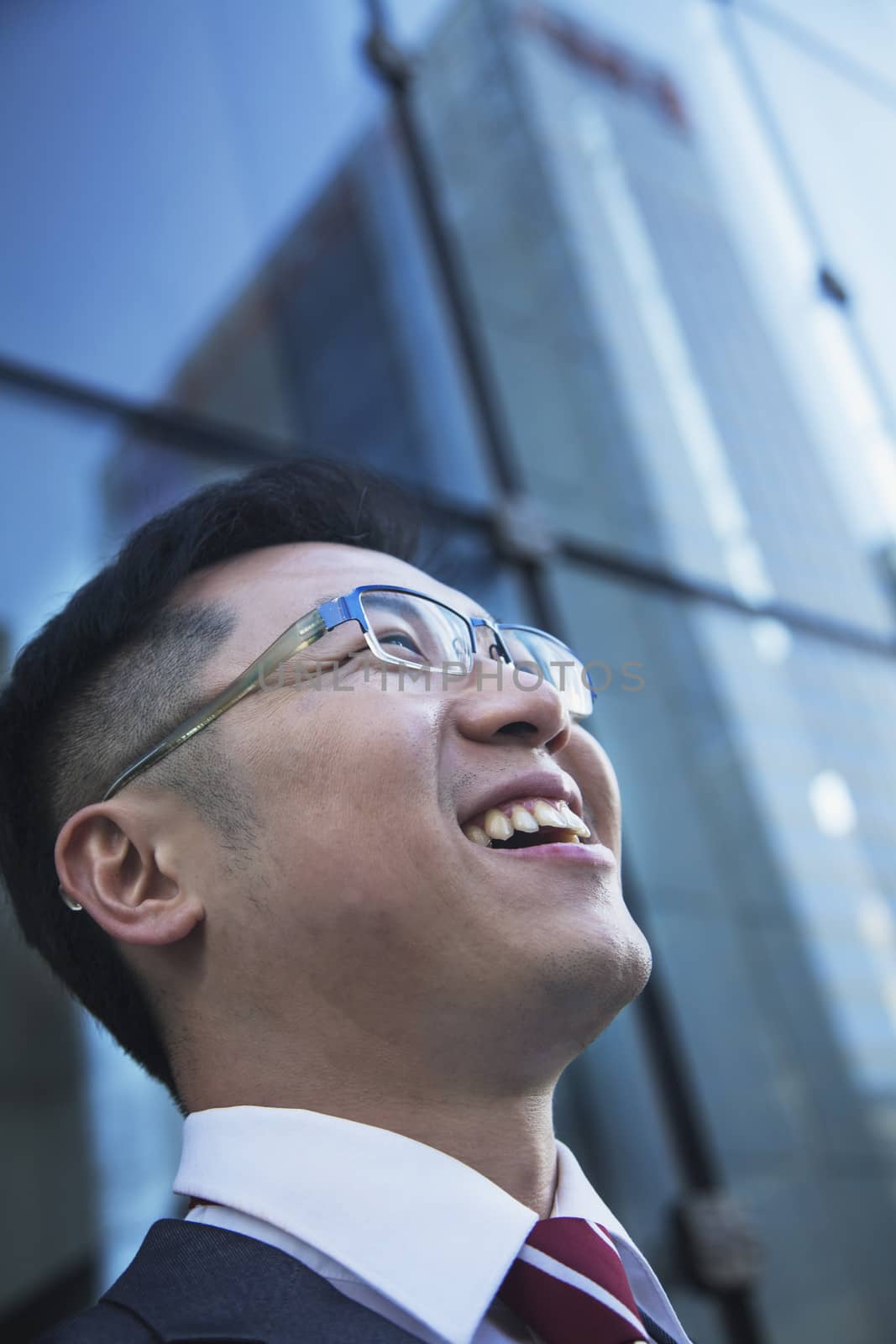 Close-up of smiling and laughing businessman looking up with glass reflection of skyscraper by XiXinXing