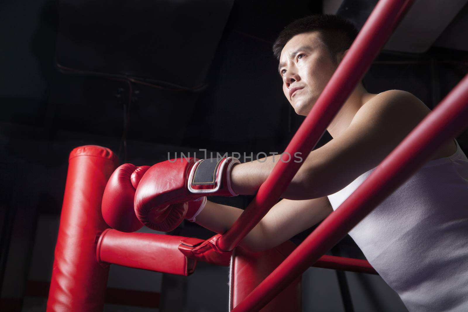Serious male boxer resting his elbows on the ring side, looking away, low angle view