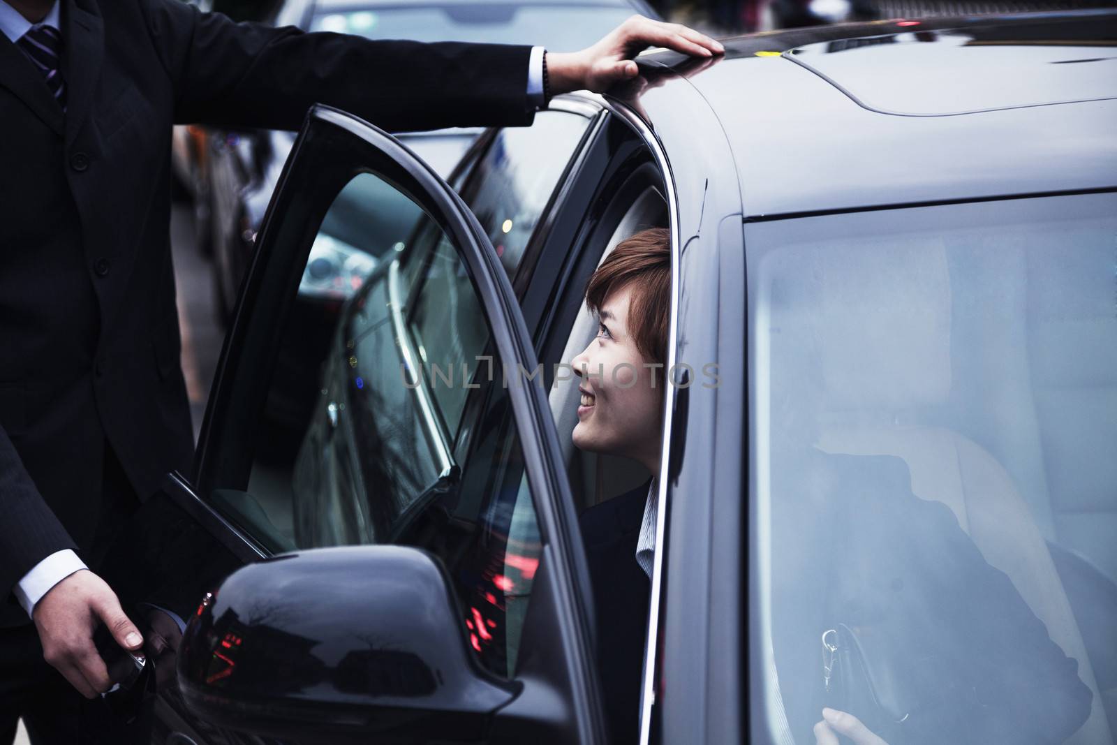 Businessman opening car door for businesswoman during the day in Beijing by XiXinXing