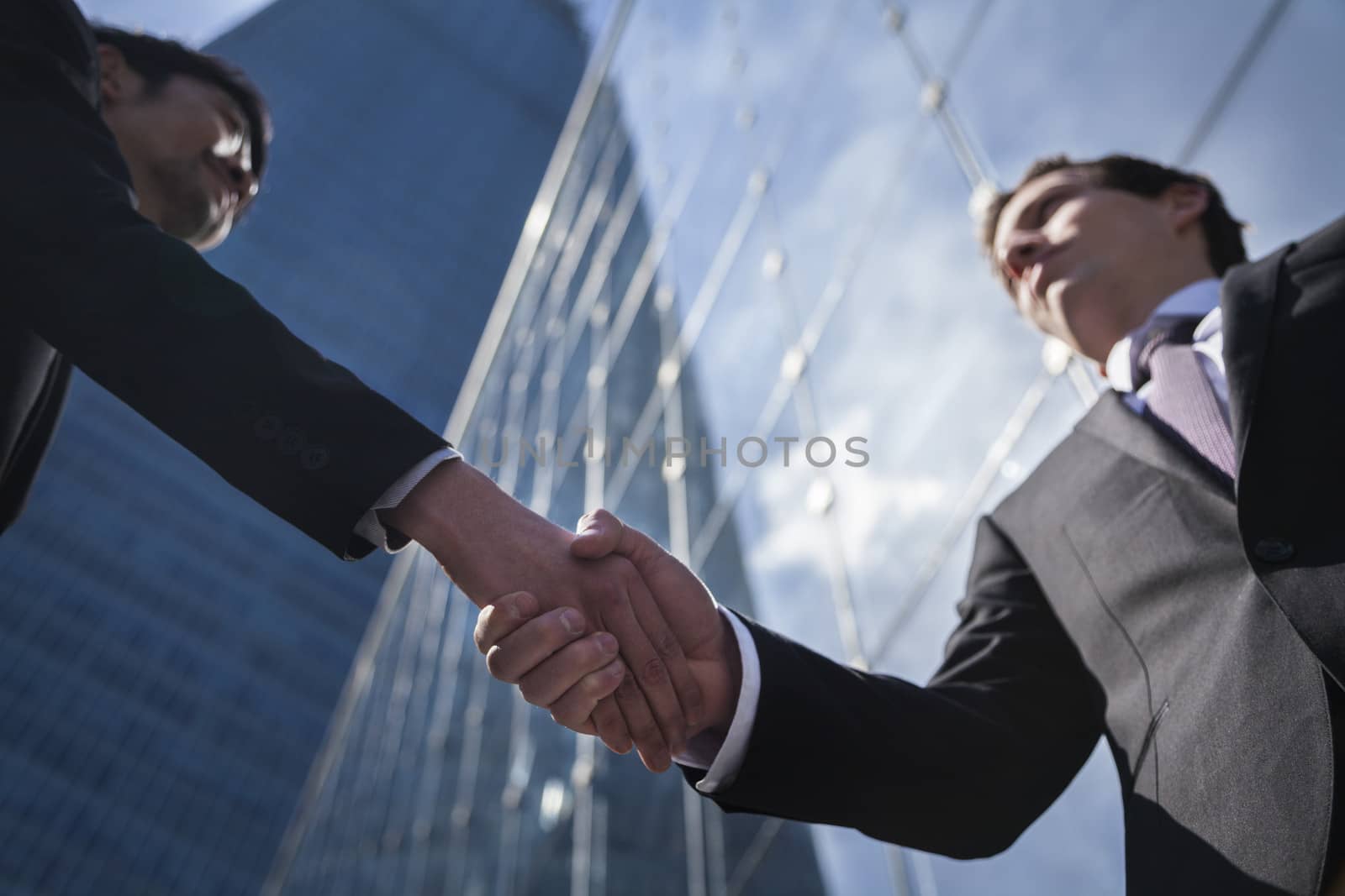 Two businessmen shaking hands in Beijing, China, view from below by XiXinXing