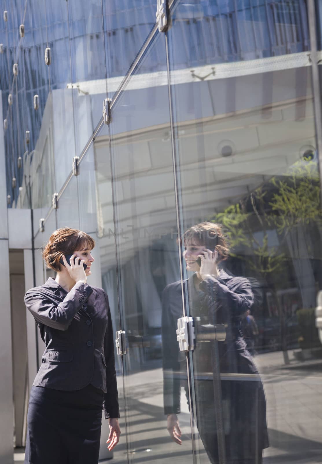 Smiling businesswoman on the phone outside in Beijing looking at her reflection in the glass of the building