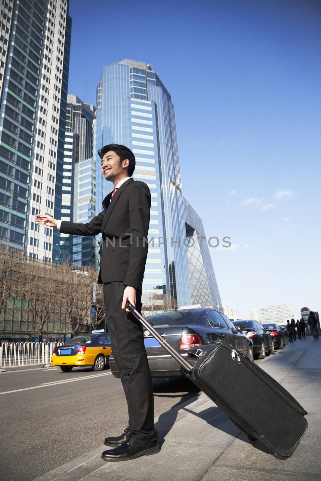 Young Businessman with luggage on the street hailing a cab 